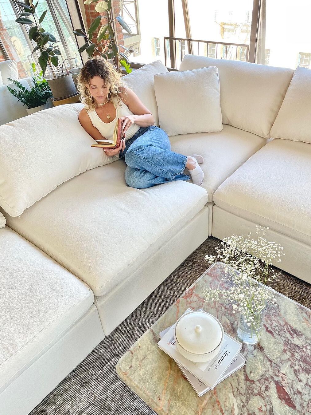 A model laying back reading a book on a pale cream 7th Avenue modular couch.