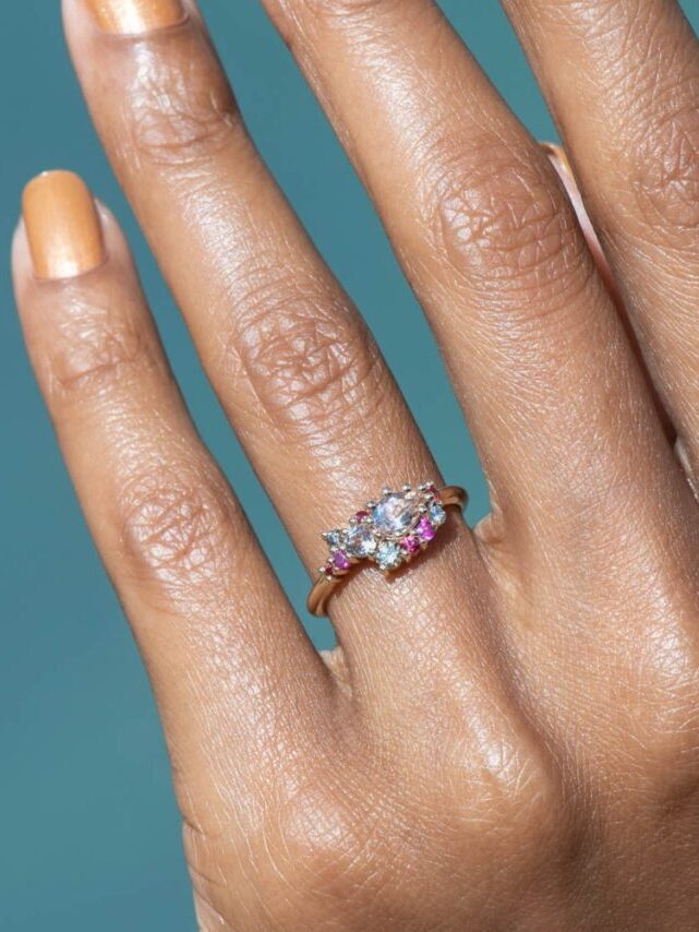 A hand shot of a clustered pink gemstone and diamond engagement ring by Bario Neal.