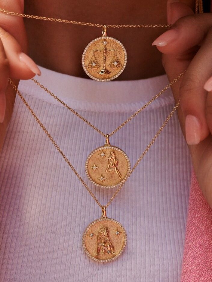 A close up shot of a model's neck wearing 3 Brilliant Earth zodiac pendant necklaces in gold.
