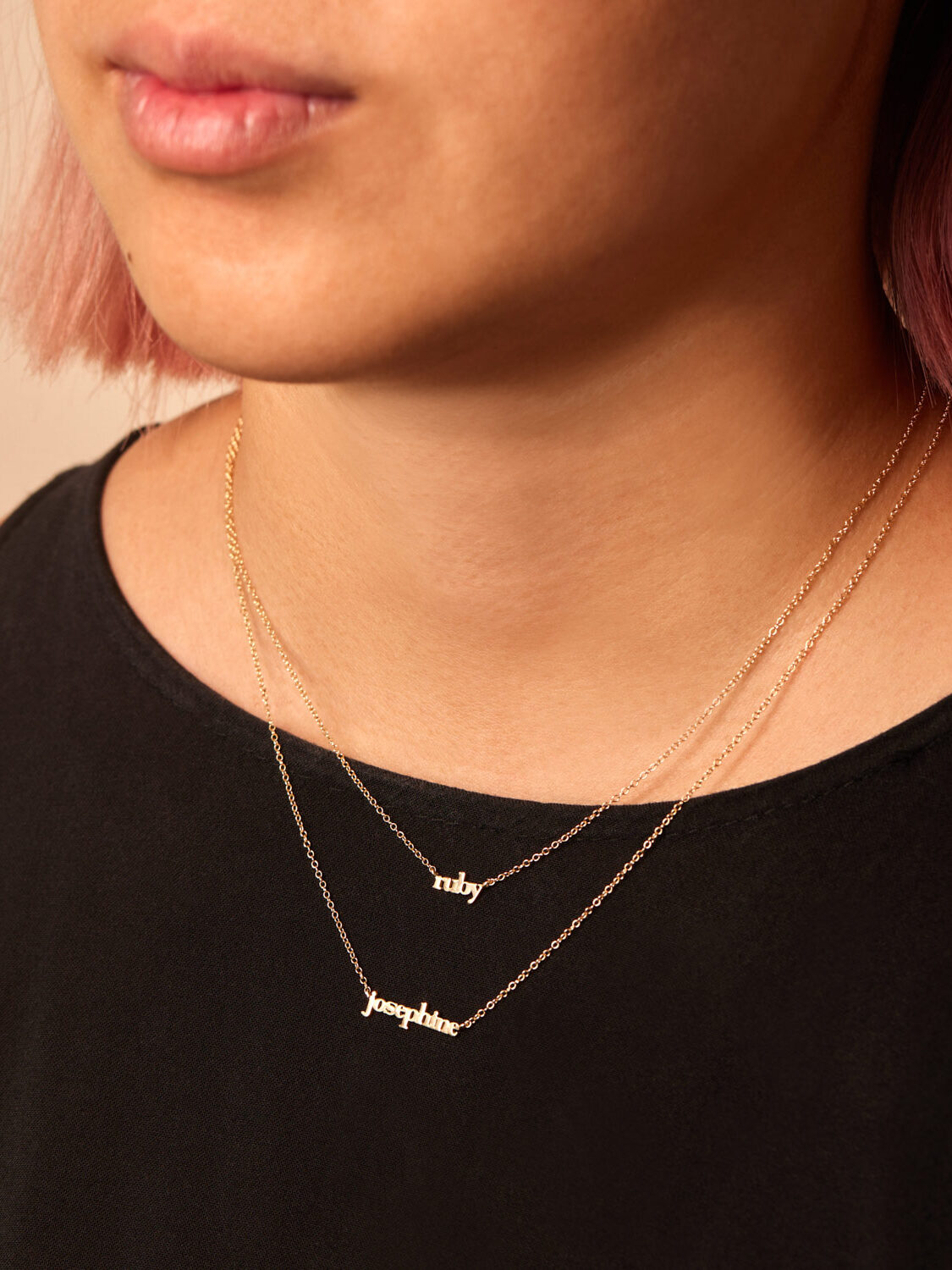 A close up shot of a model wearing two name necklaces in gold by Catbird.
