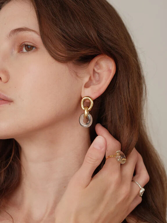 A model wearing chunky gold and glass earrings and rings by CLED.