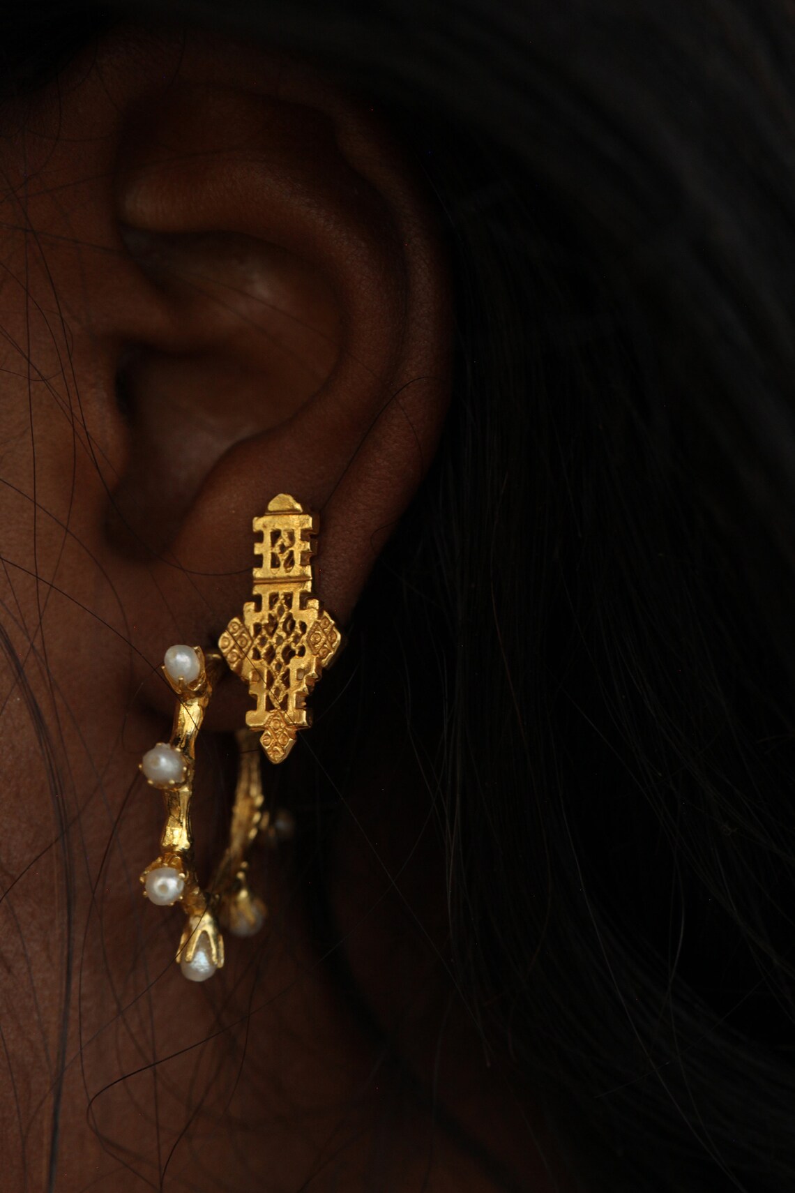 A close up shot of a model's ears wearing two earrings, one a gold hoop with pearls, and another large gold stud by Etsy shop Omi Woods.