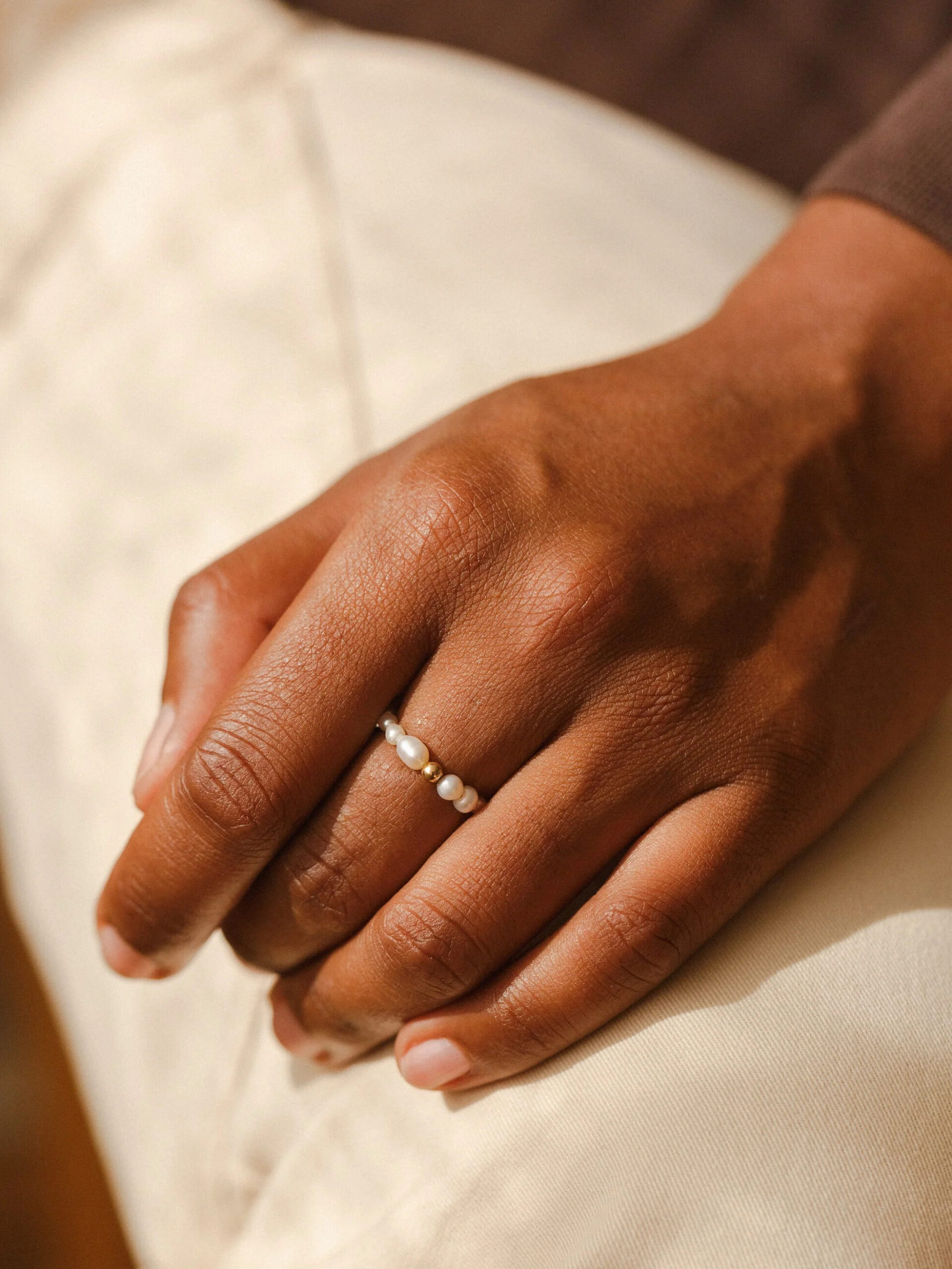 A close up studio shot of a model's hand wearing a pearl ring by GLDN.