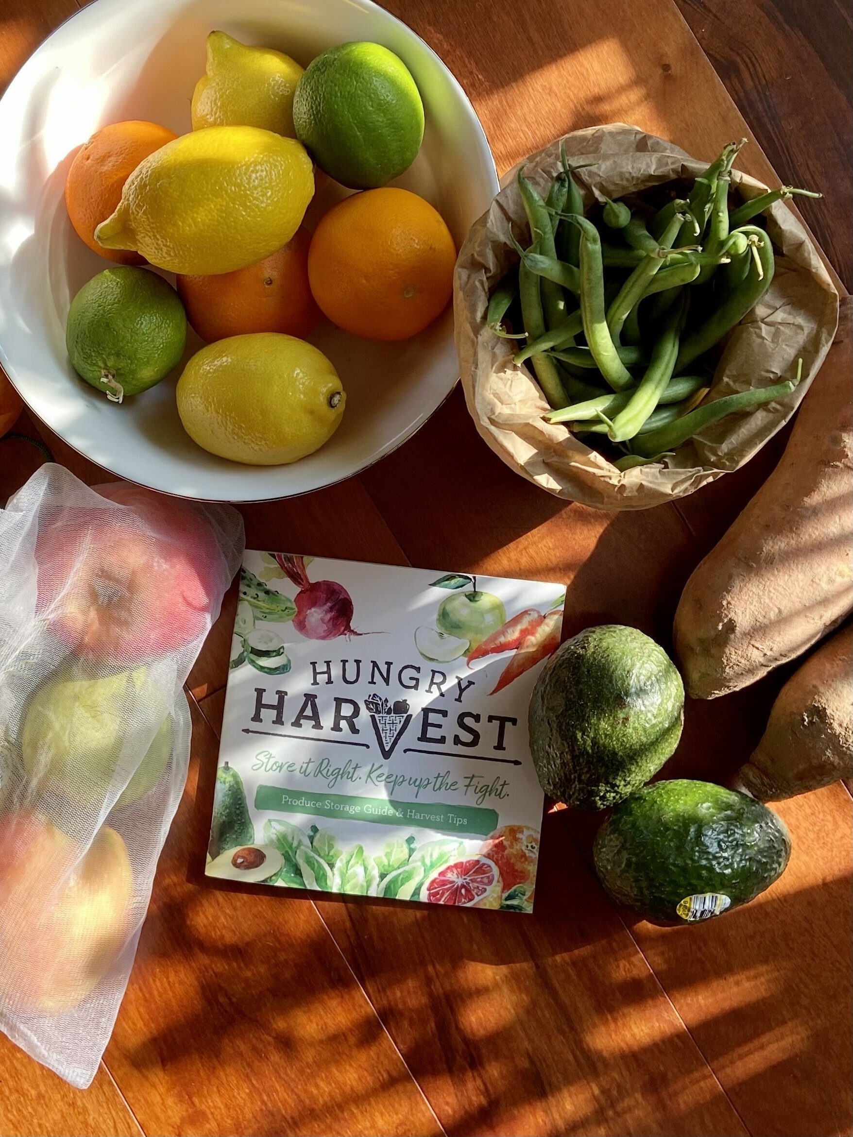 An overhead shot of a table with a bowl of fruit and vegetables and a piece of paper that says Hungry Harvest on it.