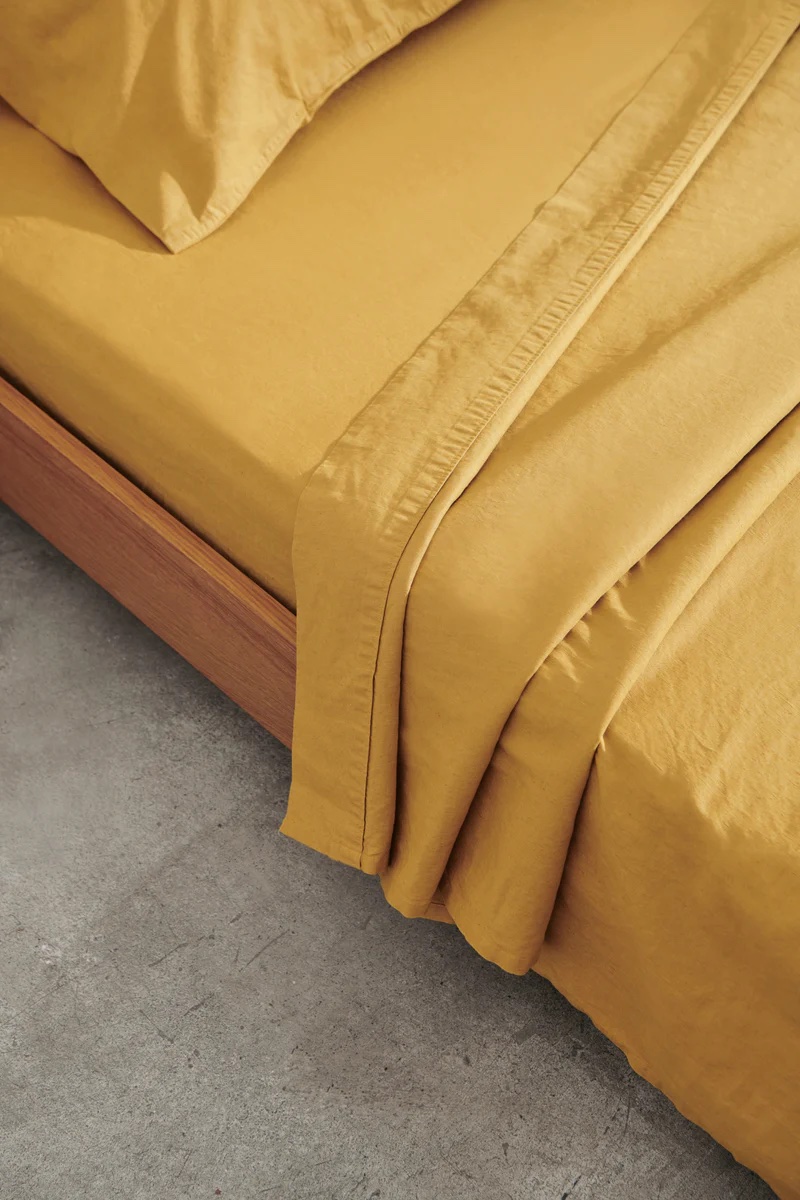 Mustard linen sheets on a made bed.