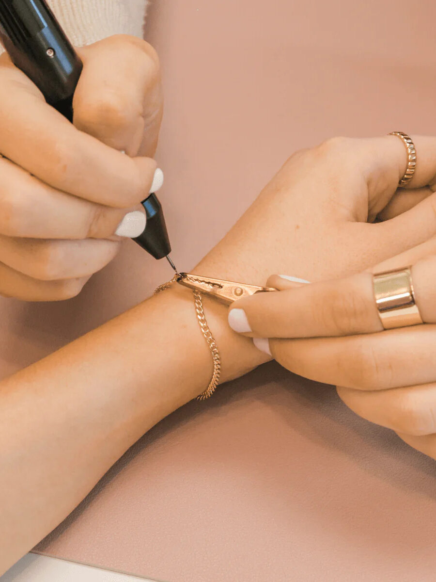 A close up shot of a model getting a permanent gold bracelet by Made by Mary zapped on.