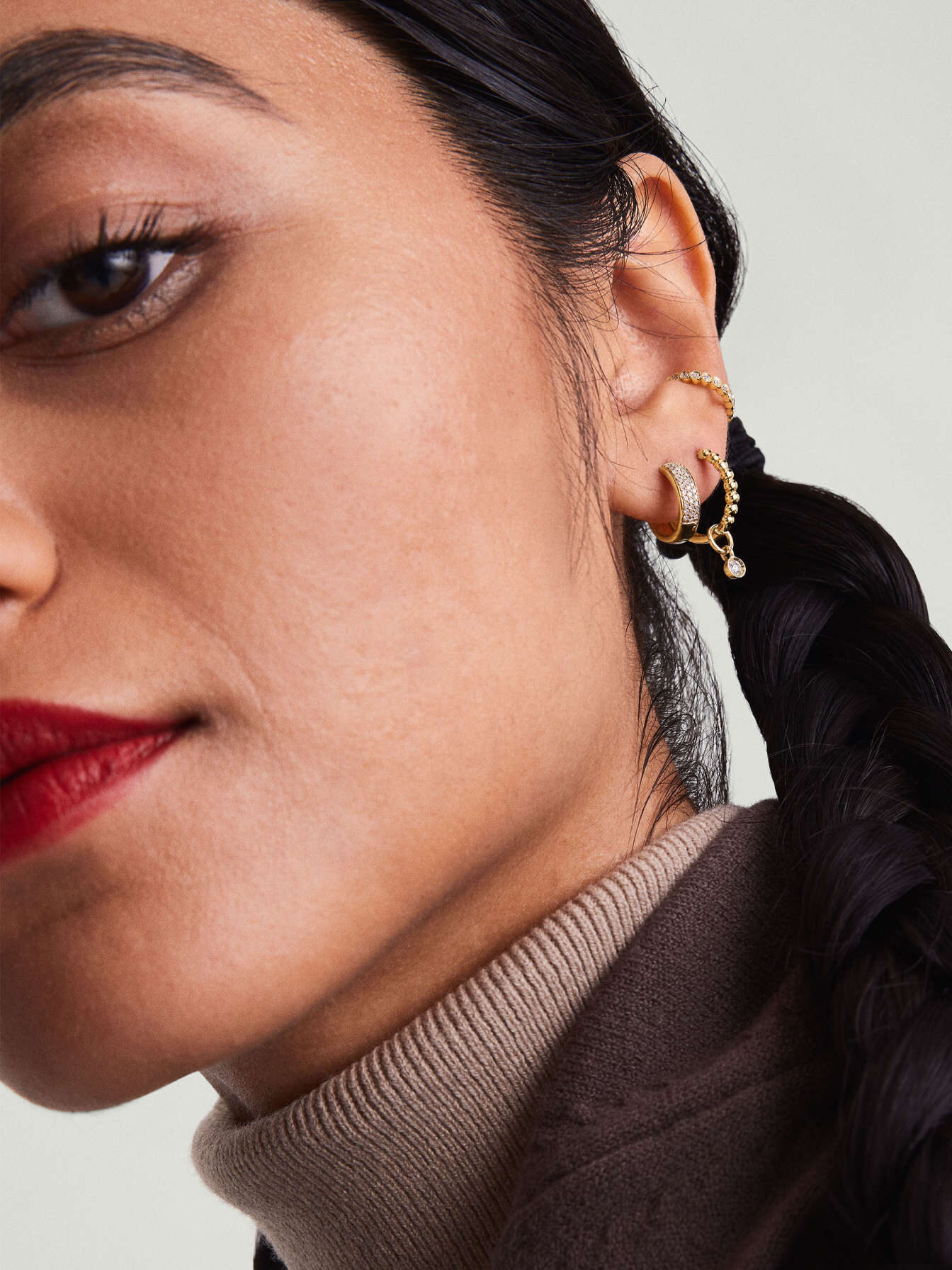 A studio shot of a model wearing 3 Mejuri small good hoop earrings with diamond accents on one ear.
