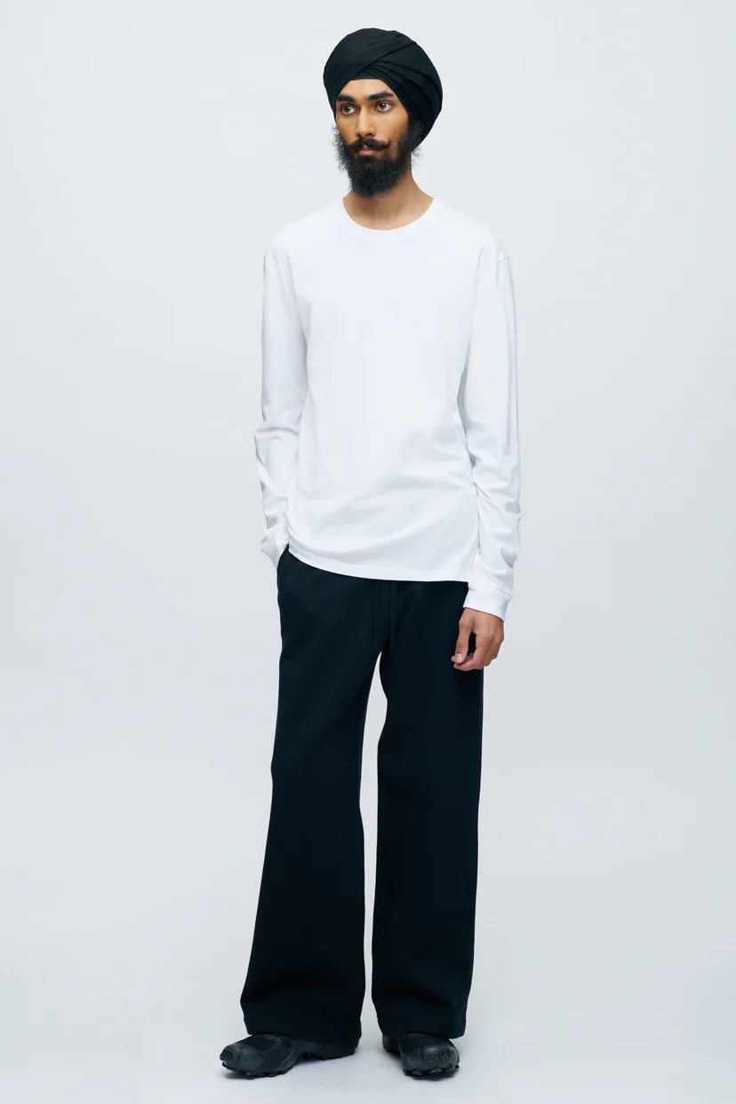 A model in a white long sleeved shirt, black pants.