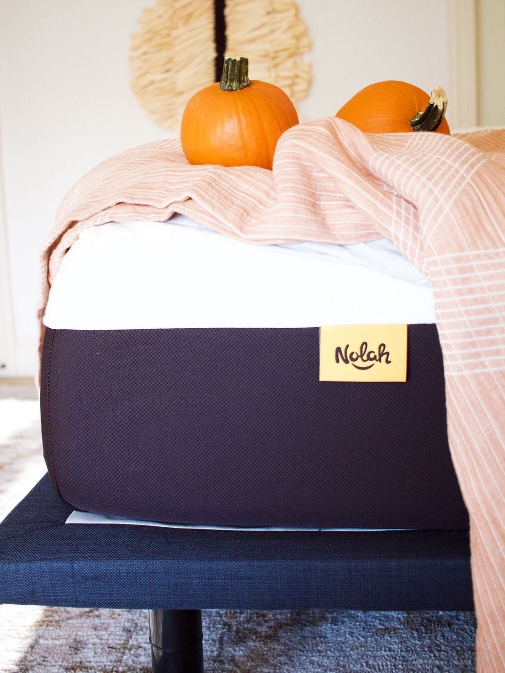 Two pumpkins and a pale red and white striped blanked on a Nolah mattress.