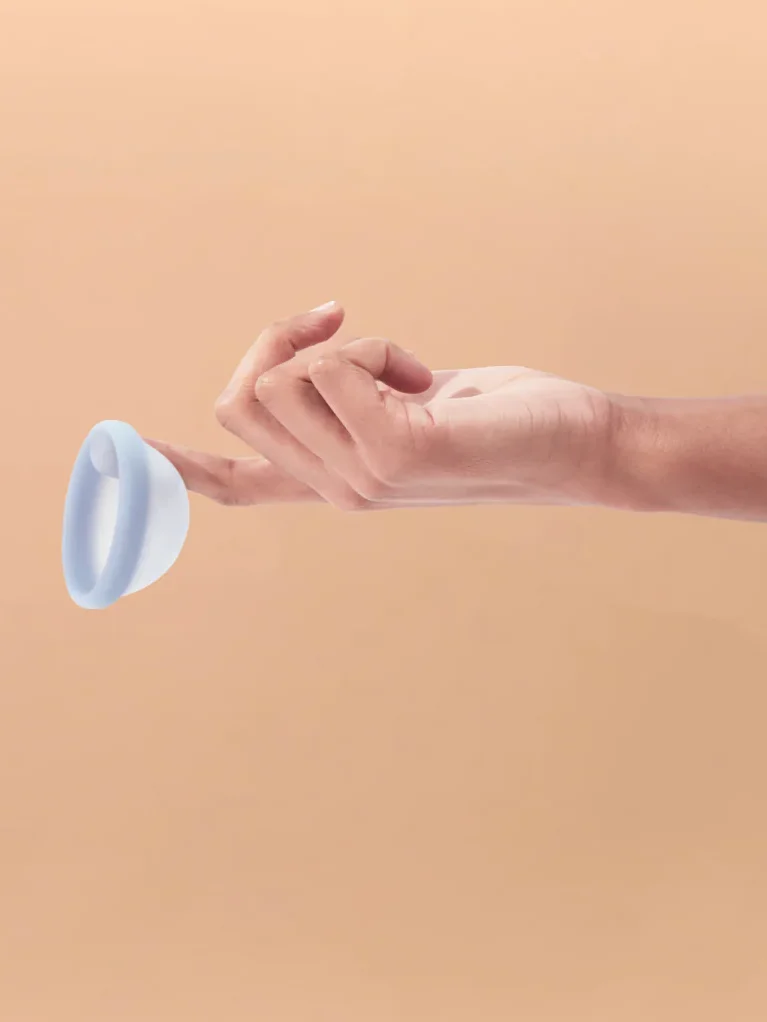 A hand holds out a blue Saalt menstrual disc