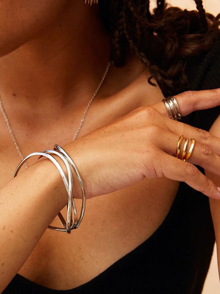 A close up shot of a model's hand and neck, wearing silver and gold SOKO rings and silver SOKO bangle bracelets.