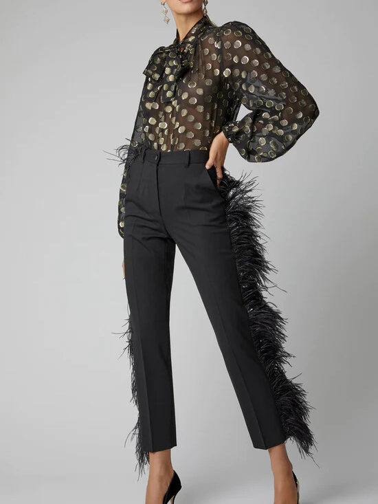 A model wearing a sheer patterned black blouse and black trousers with feathers on the sides from Tulerie.